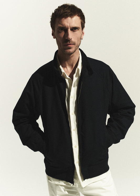 Man wearing a navy jacket over a white shirt on a plain background
