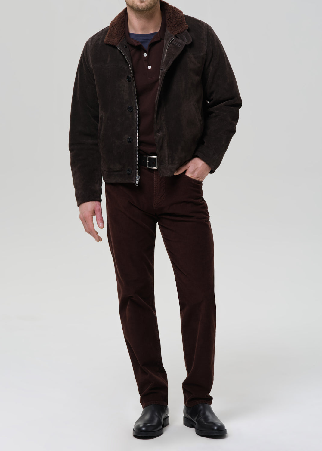 Man wearing a brown jacket, shirt, pants, and shoes on a grey background