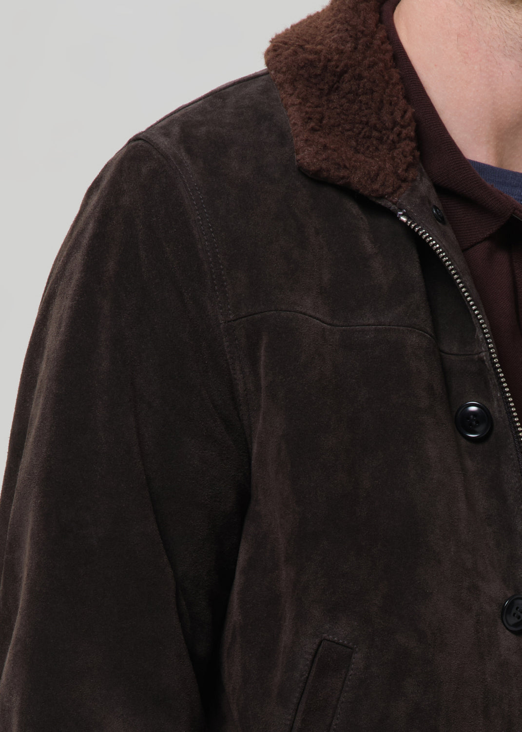 Close-up of a brown jacket with a fur-lined collar on a grey background