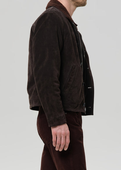 Man wearing a brown jacket and pants against a grey background