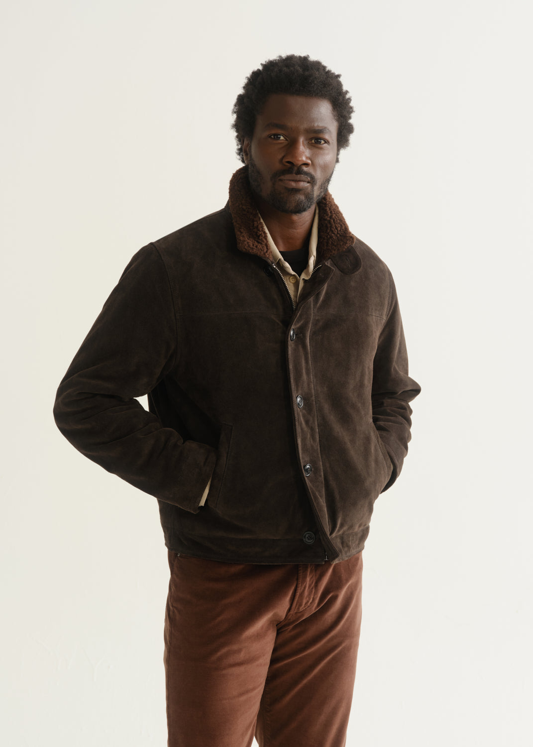 Person wearing a dark brown jacket over a dark shirt with rust brown pants, front cropped view on a light grey background.