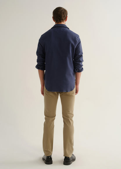Person wearing a navy long sleeve button-up shirt with khaki pants and black shoes, back full body view on a light grey background.