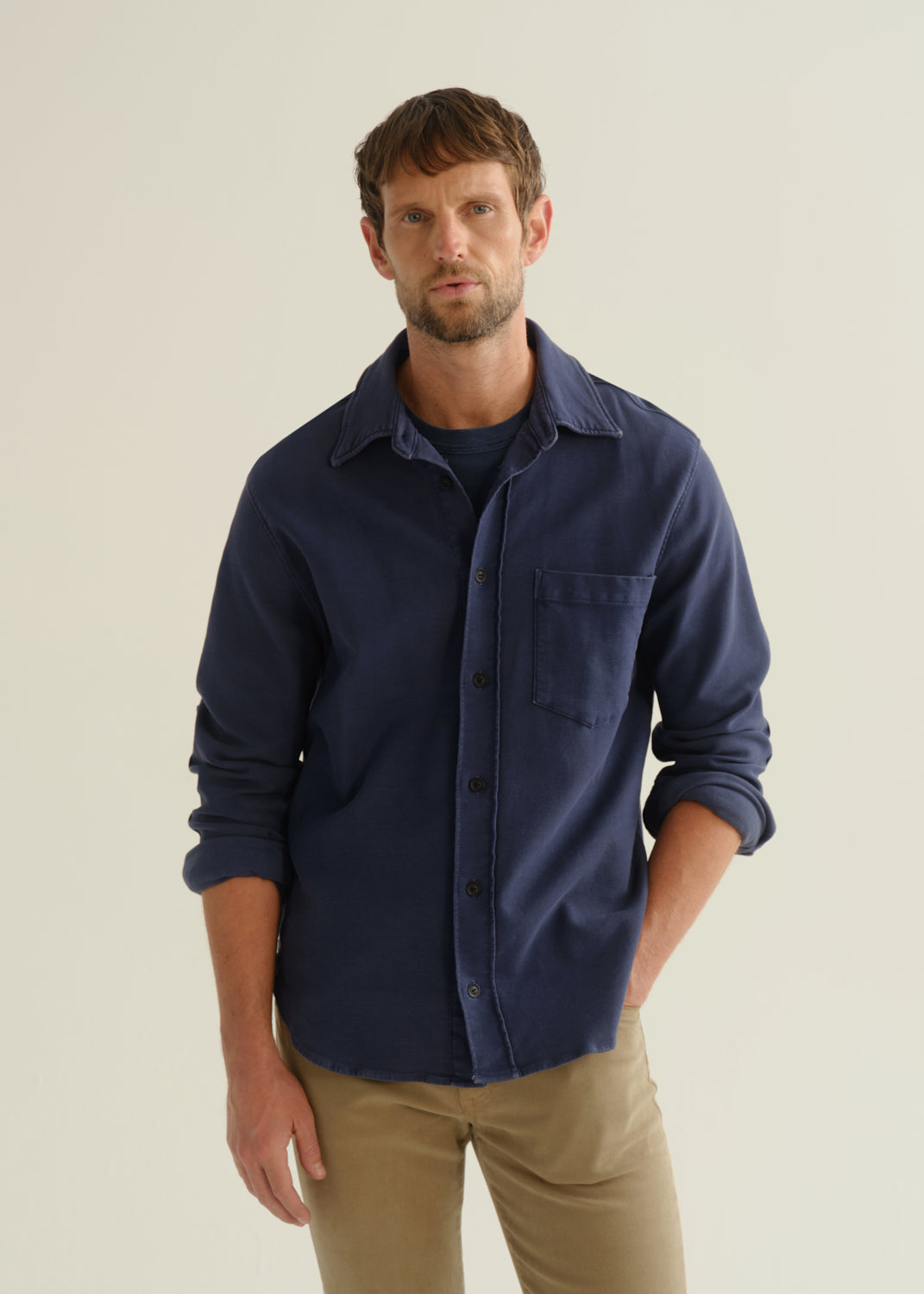 Person wearing a navy long sleeve button-up shirt with khaki pants, angled front cropped view on a light grey background.