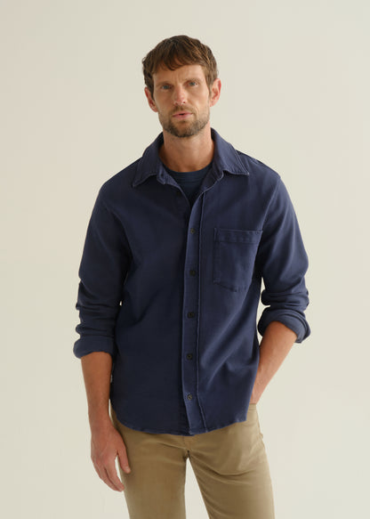 Person wearing a navy long sleeve button-up shirt with khaki pants, angled front cropped view on a light grey background.