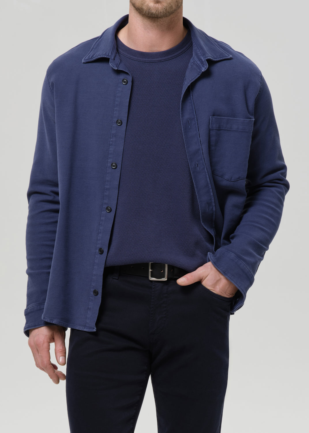 Man wearing a navy blue shirt over a dark t-shirt with a grey background