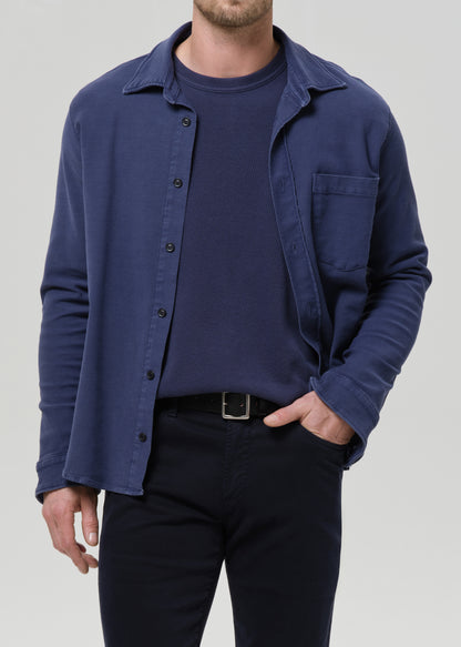 Man wearing a navy blue shirt over a dark t-shirt with a grey background