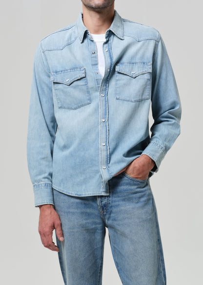 Person wearing a light blue denim shirt and jeans on a plain background