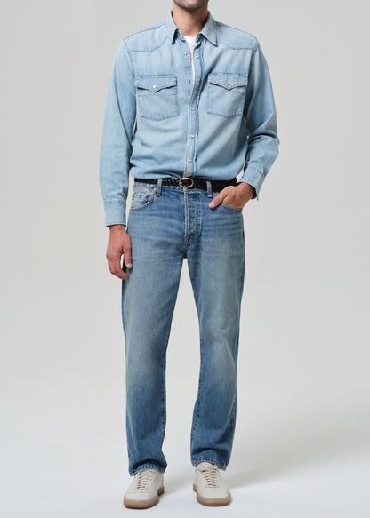 Person wearing a light blue denim shirt and jeans on a plain background