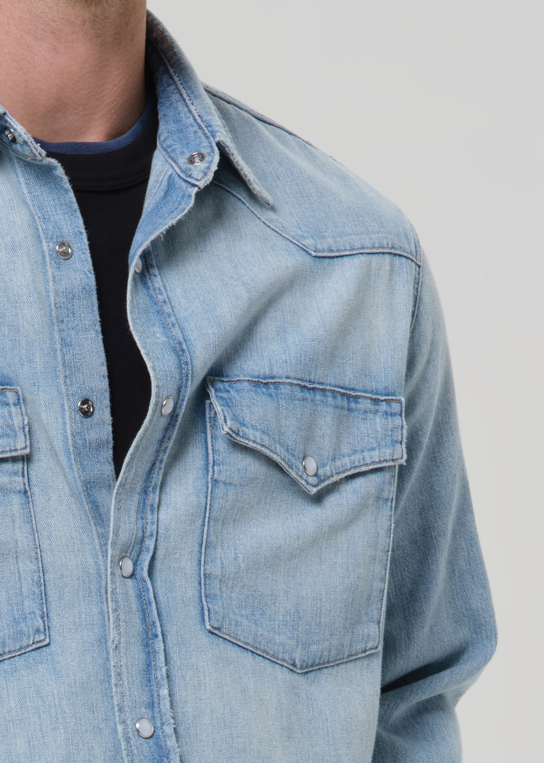A man wearing a light blue denim western shirt, photographed against a grey background.