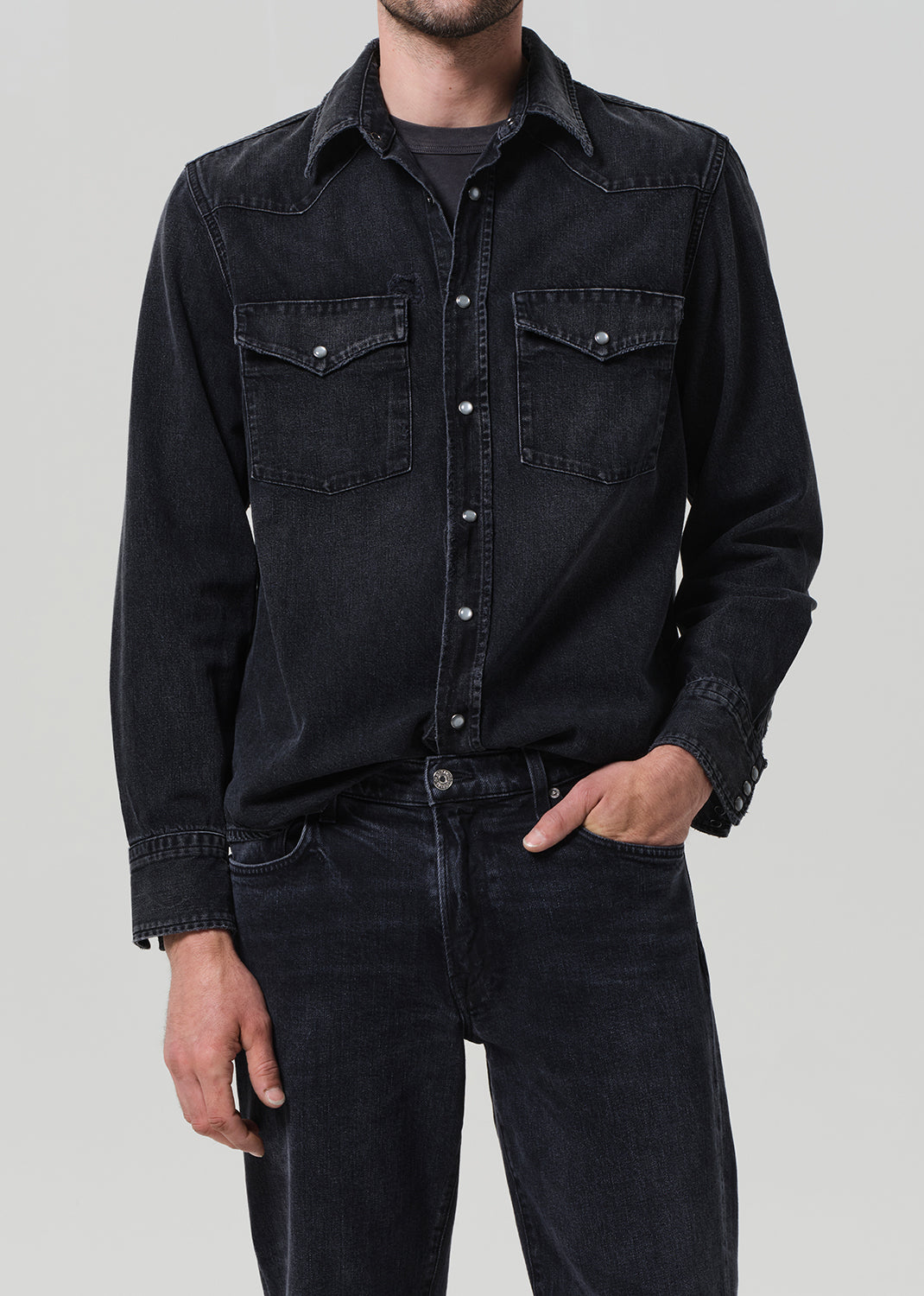 Person wearing a black denim shirt and jeans on a gray background