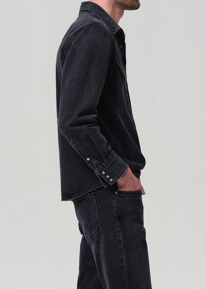 Person wearing a black denim jacket and jeans on a plain background