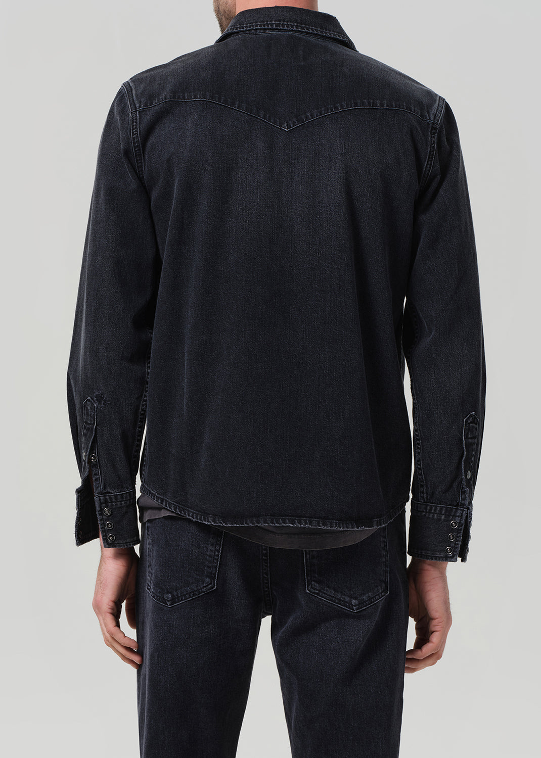 Person wearing a black denim jacket and pants on a plain background