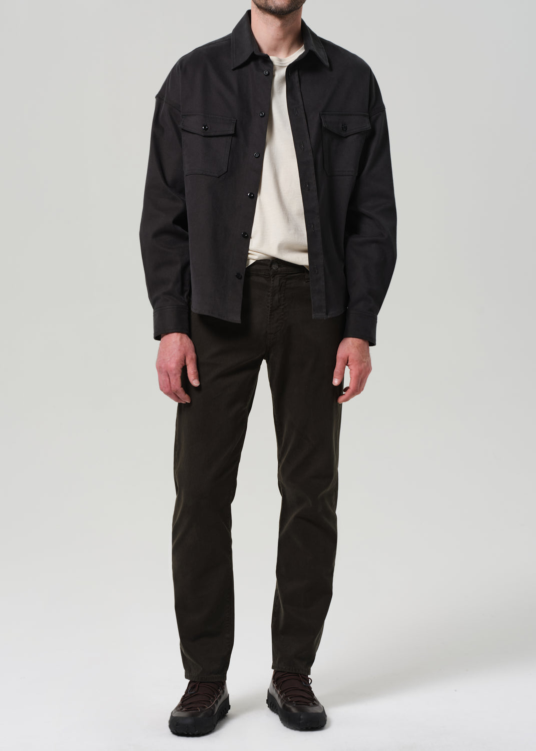 Person wearing a black shirt, white tee, and green pants on a plain background.