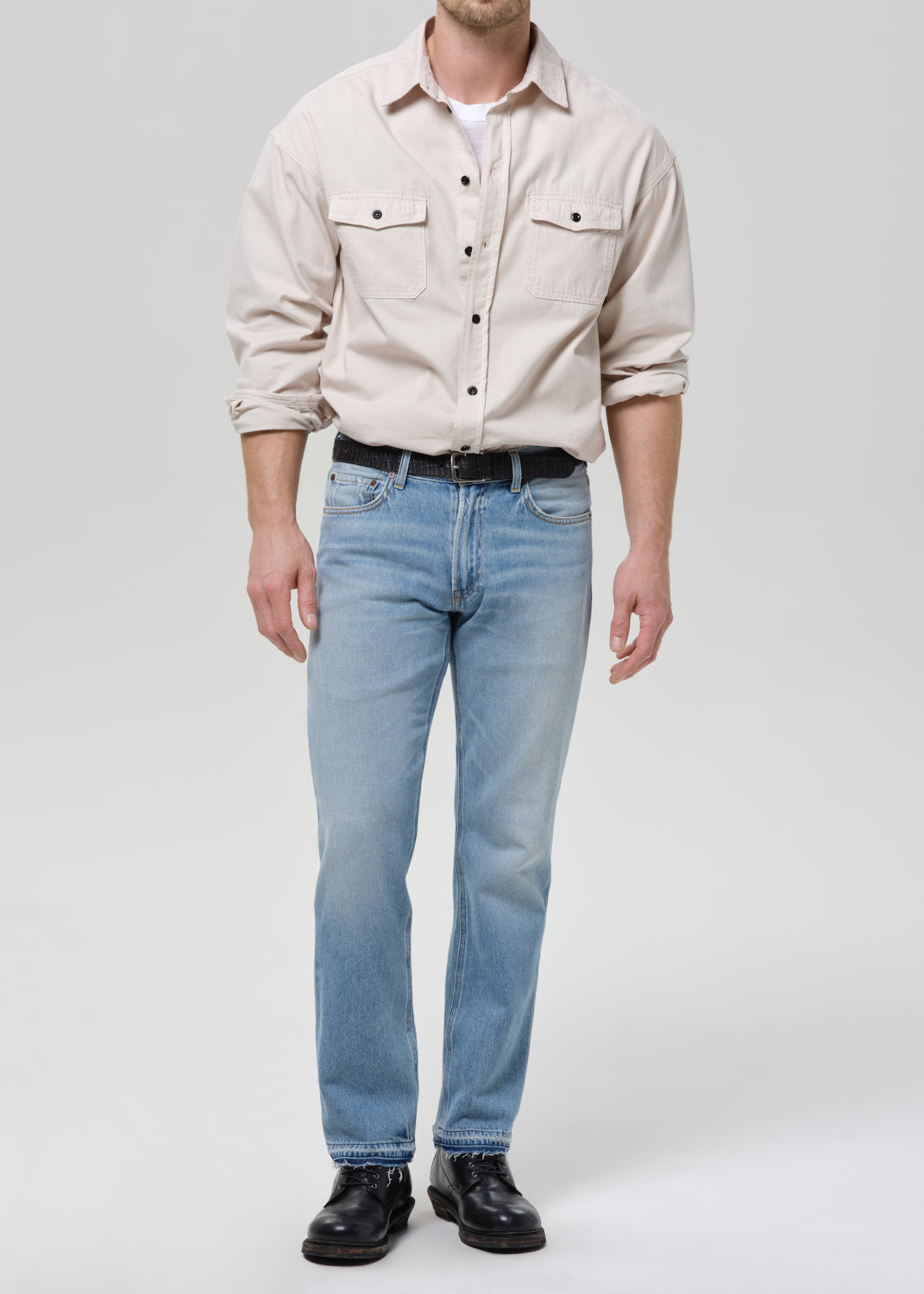 Person wearing a beige shirt and light blue jeans on a grey background.