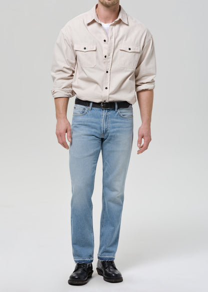 Person wearing a beige shirt and light blue jeans on a grey background.
