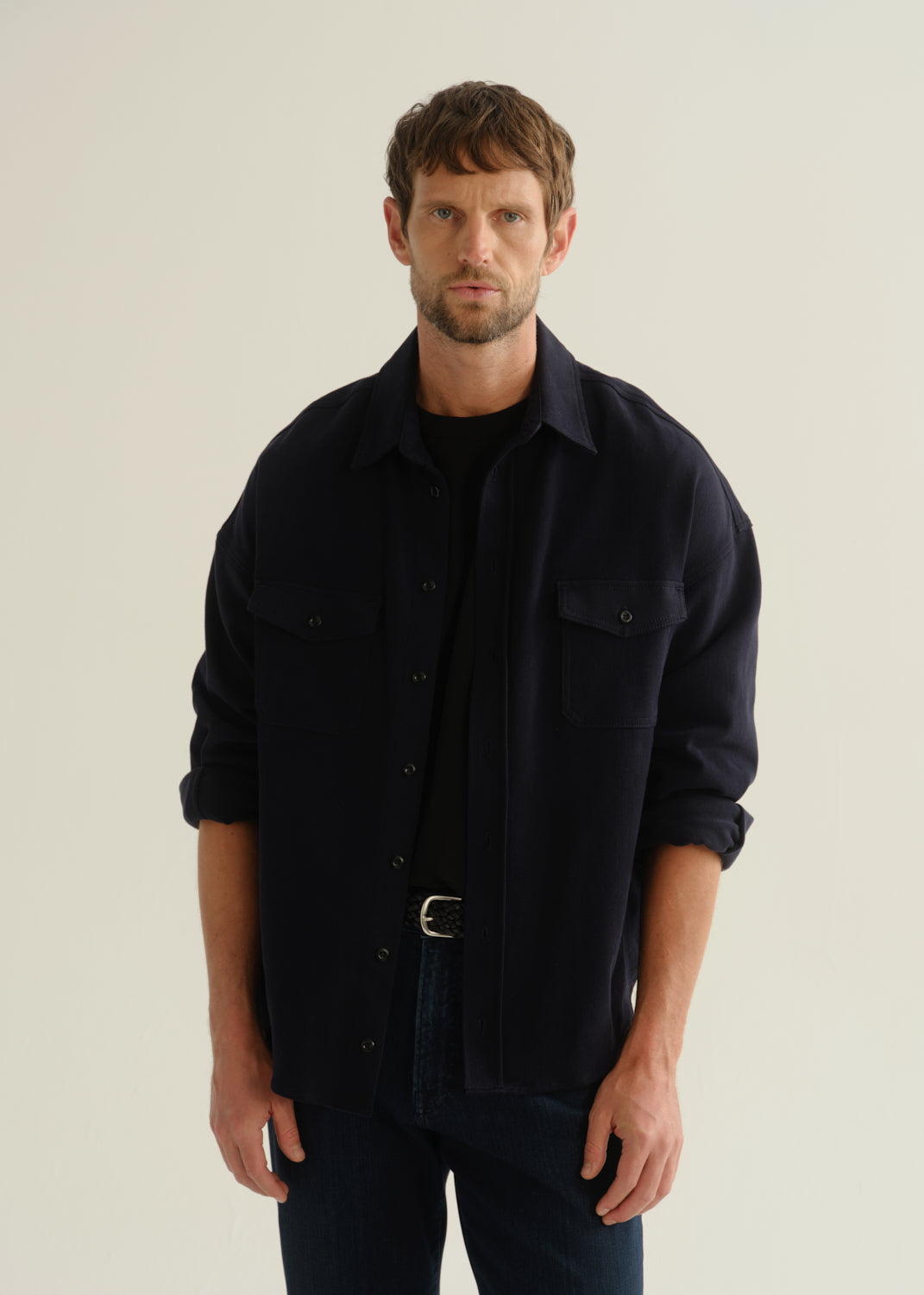 Person wearing a dark navy long sleeve button-up shirt with dark blue jeans, front cropped view on a light grey background.