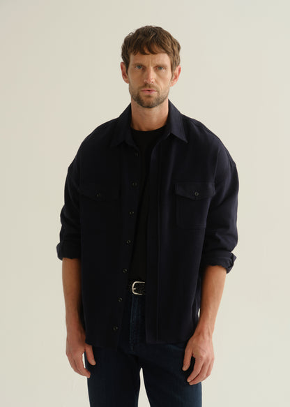 Person wearing a dark navy long sleeve button-up shirt with dark blue jeans, front cropped view on a light grey background.