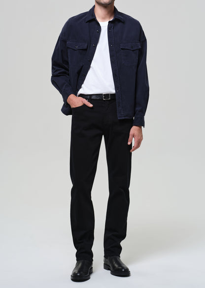 Person wearing a navy blue shirt over a white t-shirt with navy pants on a light gray background