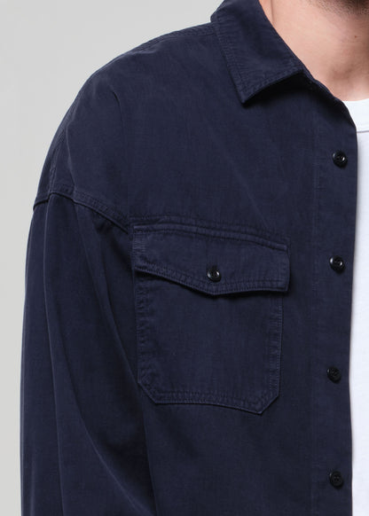 Person wearing a navy blue shirt over a white t-shirt with navy pants on a light gray background