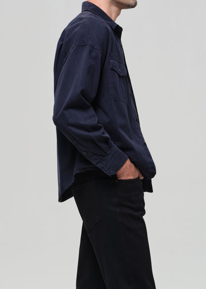 Person wearing a navy blue shirt over a white t-shirt with navy pants on a light gray background