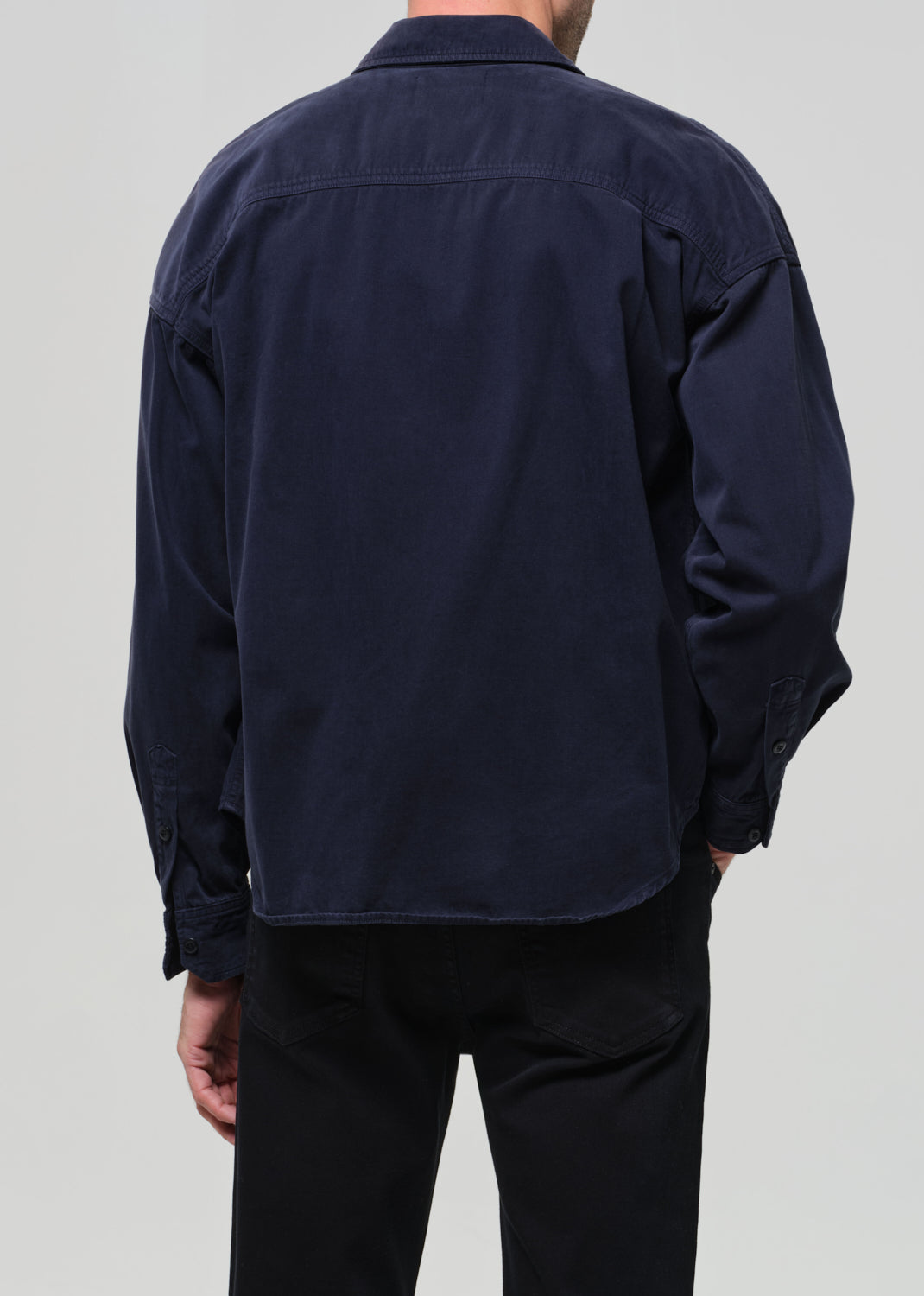 Person wearing a navy blue shirt over a white t-shirt with navy pants on a light gray background