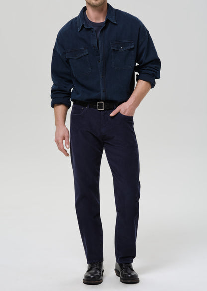 Man wearing a dark navy button-up shirt with dark navy straight leg pants on a grey background.