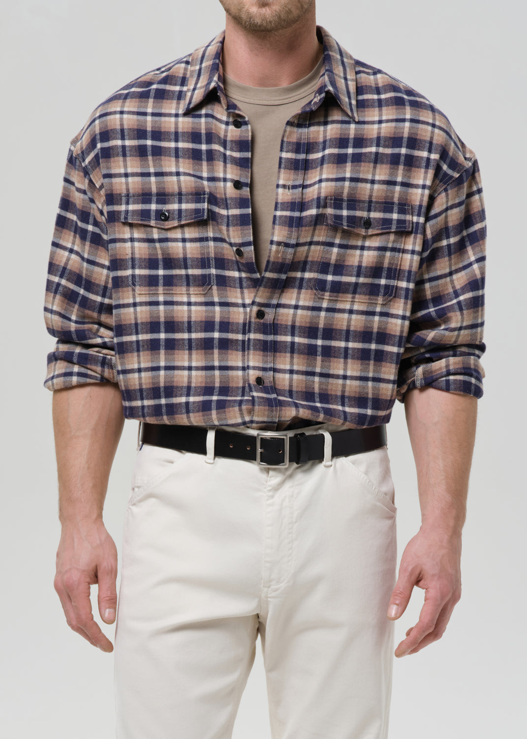 Man wearing a plaid shirt and white pants on a grey background
