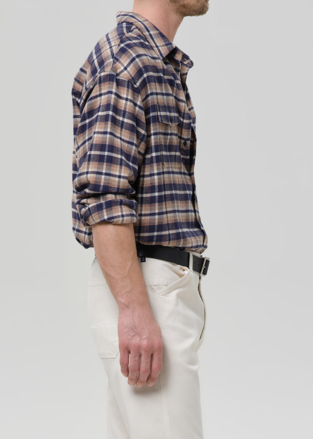Person wearing a plaid shirt and white pants on a grey background