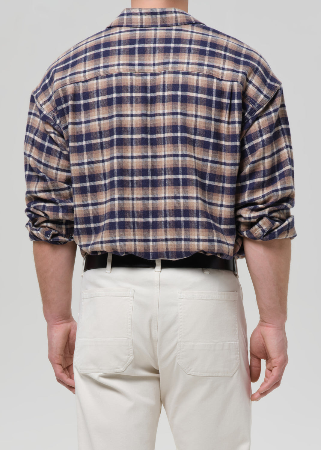 Person wearing a plaid shirt and white pants on a grey background
