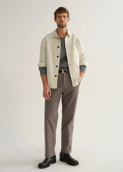 Person wearing a cream long sleeve button-up shirt over a grey top with brown pants and black boots, front full body view on a light grey background.