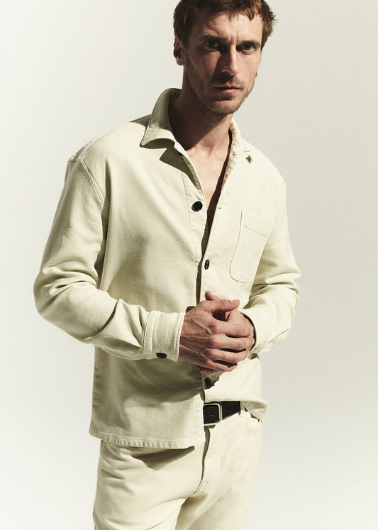 Man wearing a light-colored shirt and pants against a plain background
