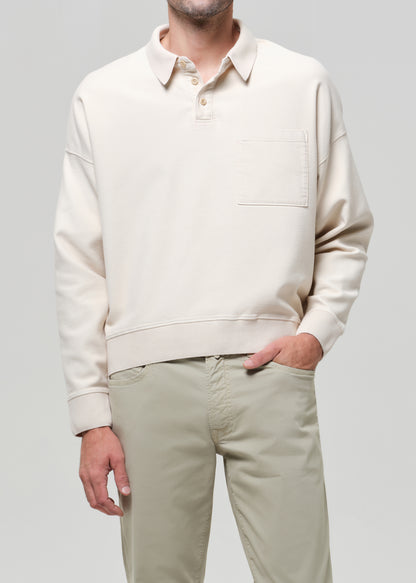 Man wearing a beige polo and light-colored pants against a gray background