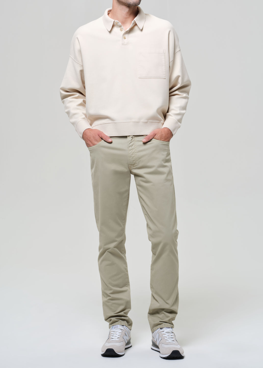 Man wearing a beige polo and light-colored pants against a gray background