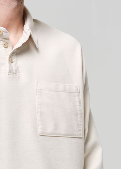 Man wearing a beige polo and light-colored pants against a gray background