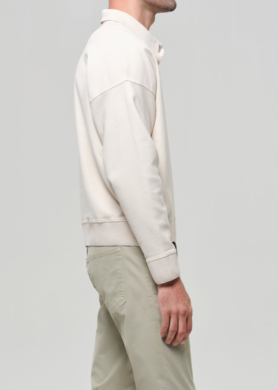 Man wearing a beige polo and light-colored pants against a gray background