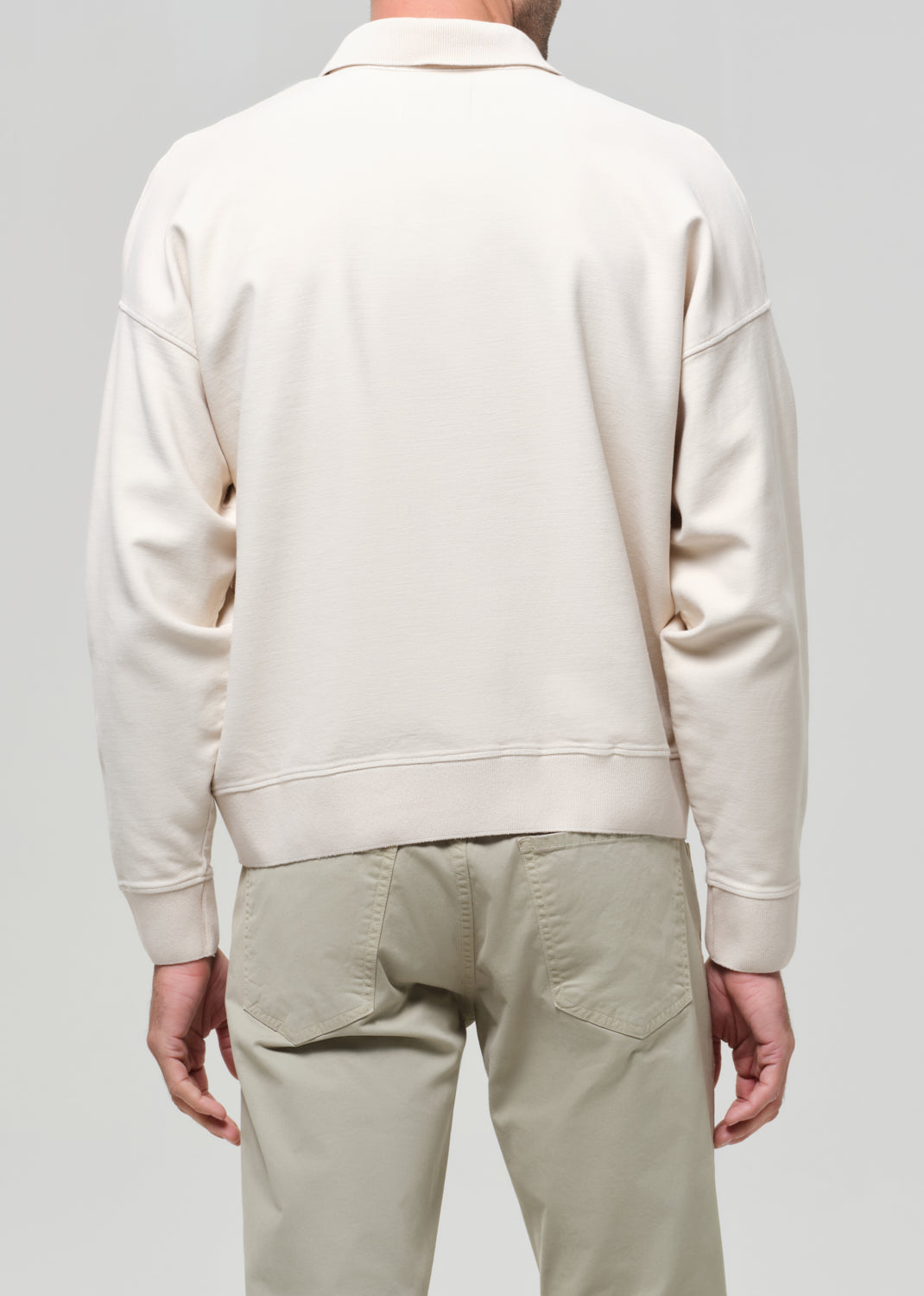 Man wearing a beige polo and light-colored pants against a gray background