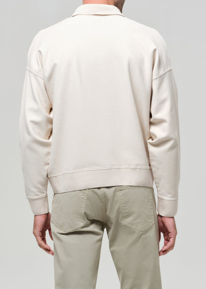 Man wearing a beige polo and light-colored pants against a gray background