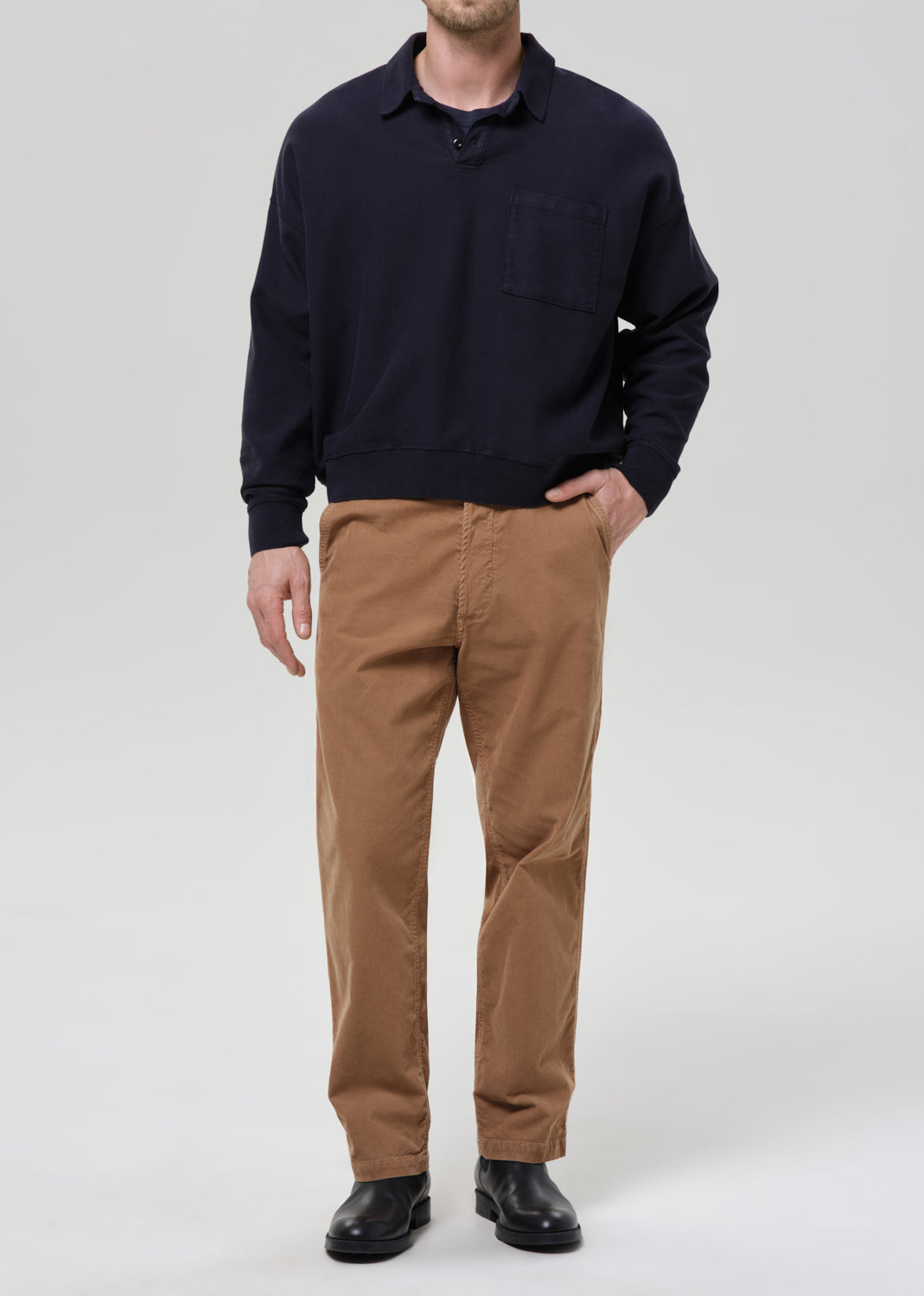 Person wearing a navy sweater and brown pants on a grey background.