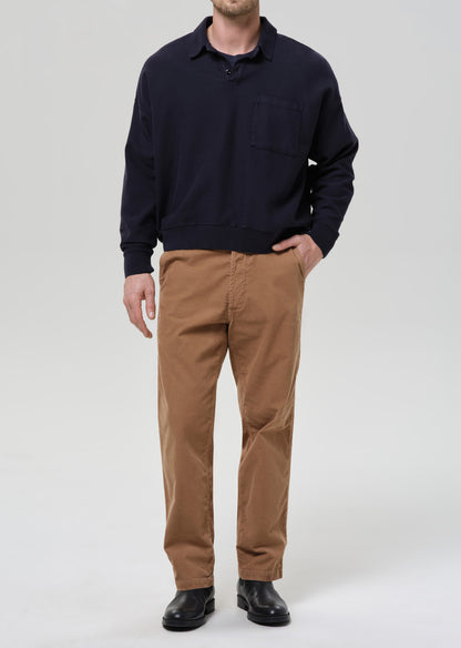 Person wearing a navy sweater and brown pants on a grey background.