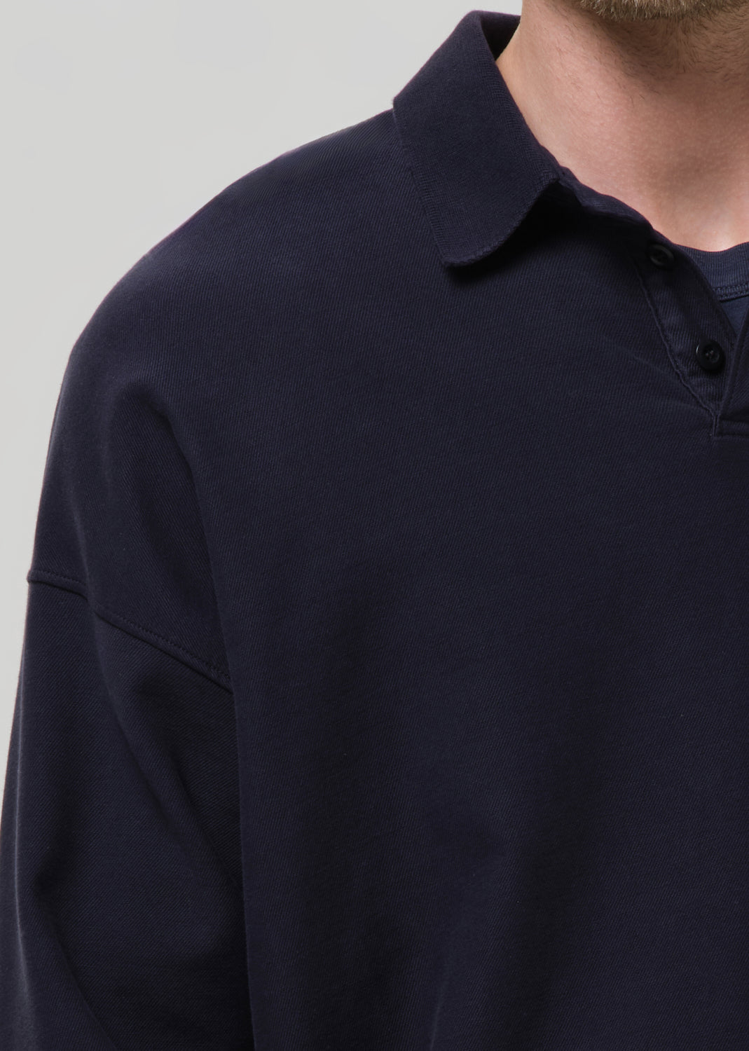 Close-up of a person wearing a dark navy long-sleeve polo shirt against a grey background.