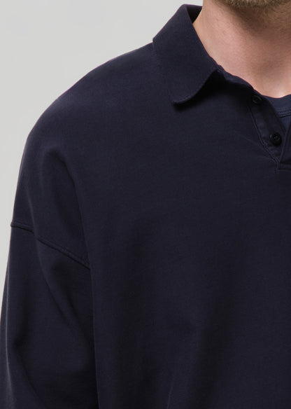 Close-up of a person wearing a dark navy long-sleeve polo shirt against a grey background.