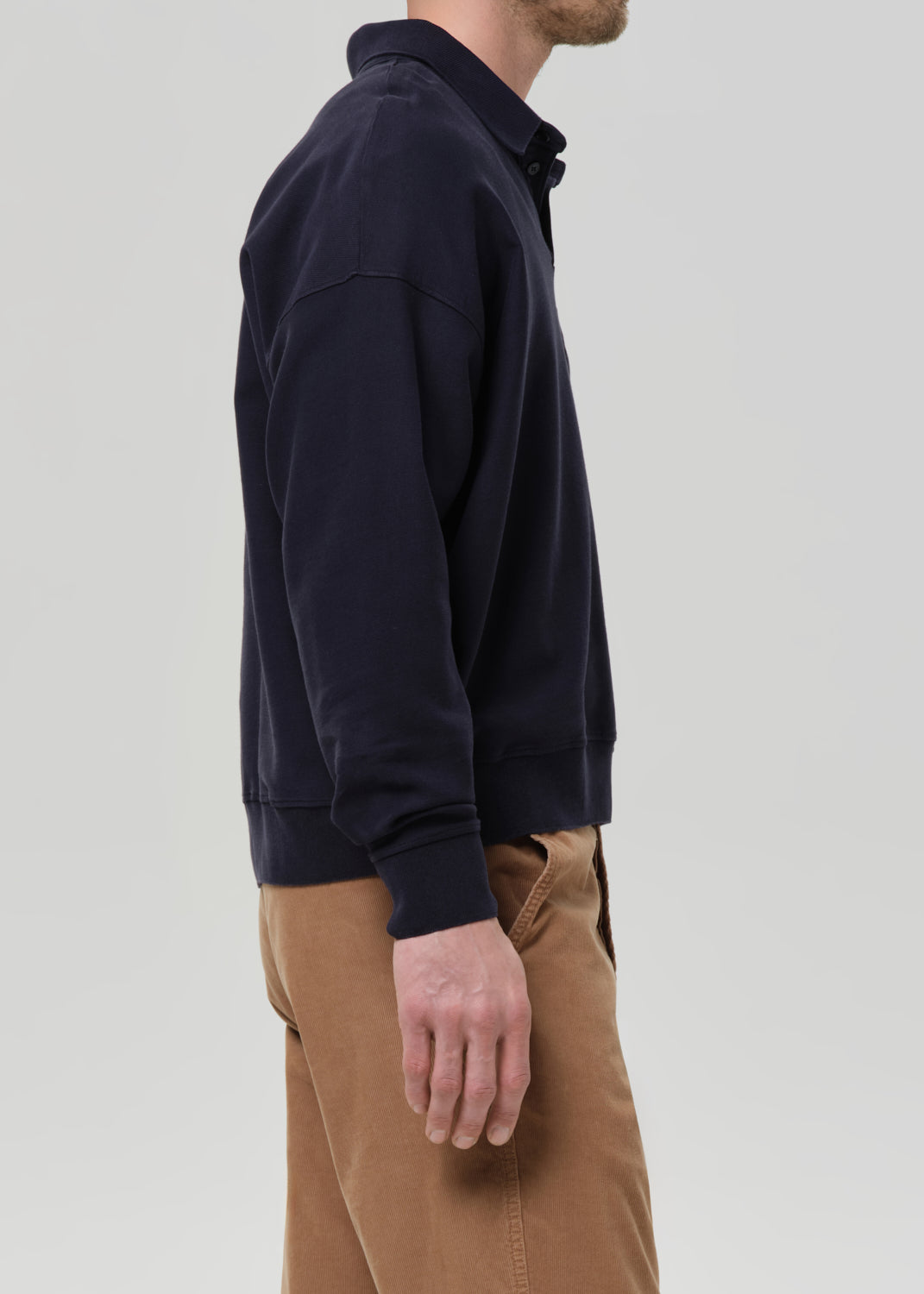 A man shown from the side wearing a dark navy long-sleeve knit polo-style top and tan pants against a grey background.