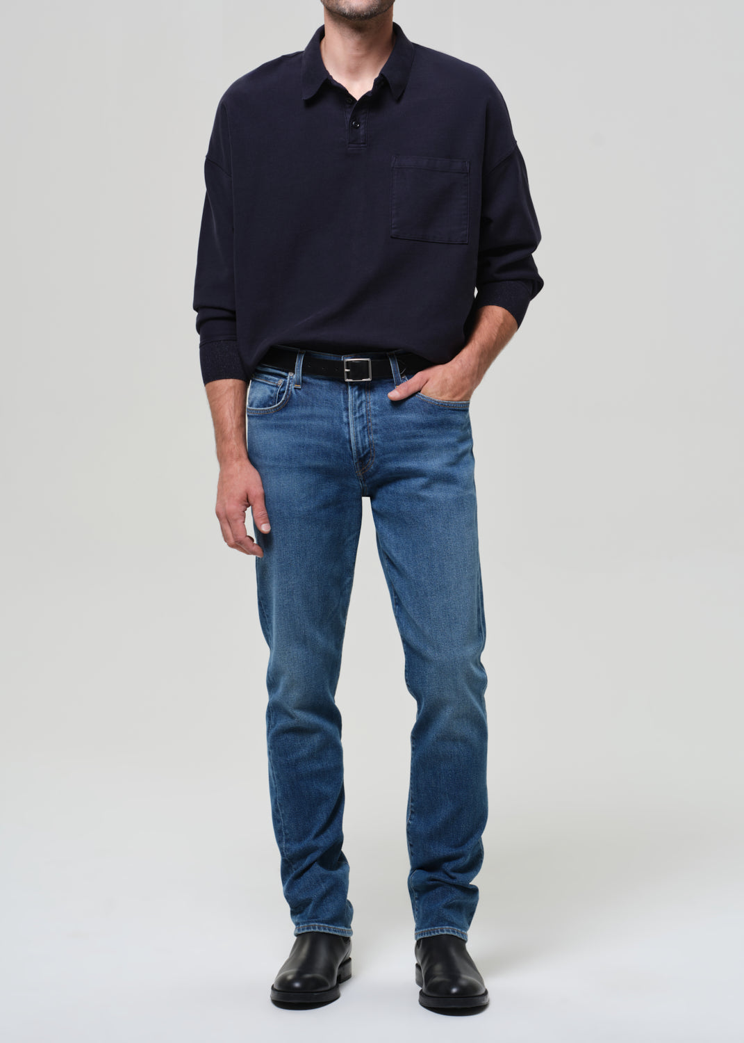 Person wearing a navy sweater, blue jeans, and black shoes on a white background