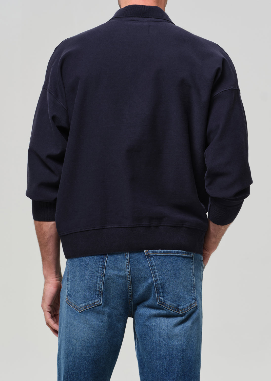 Person wearing a navy jacket and blue jeans on a light gray background