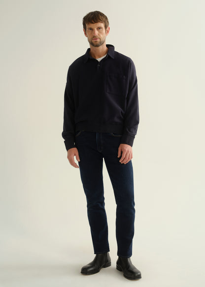 Person wearing a dark navy long sleeve collared pullover with dark blue jeans and black boots, front full body view on a light grey background.