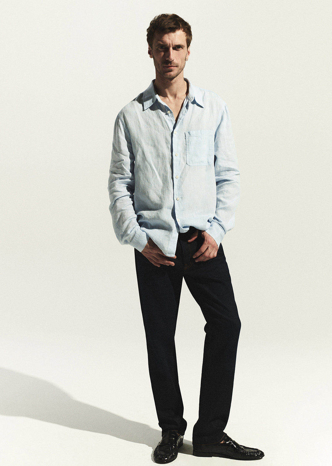 Man wearing a light blue shirt and dark wash jean on a white background