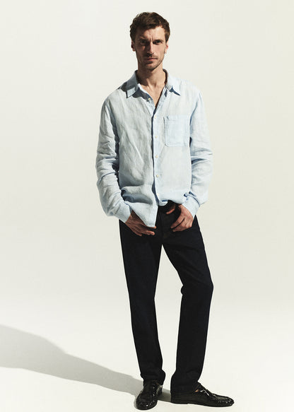 Man wearing a light blue shirt and dark wash jean on a white background