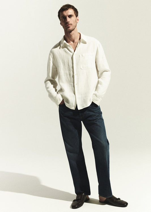 Man wearing a white shirt and dark wash jeans against a white background