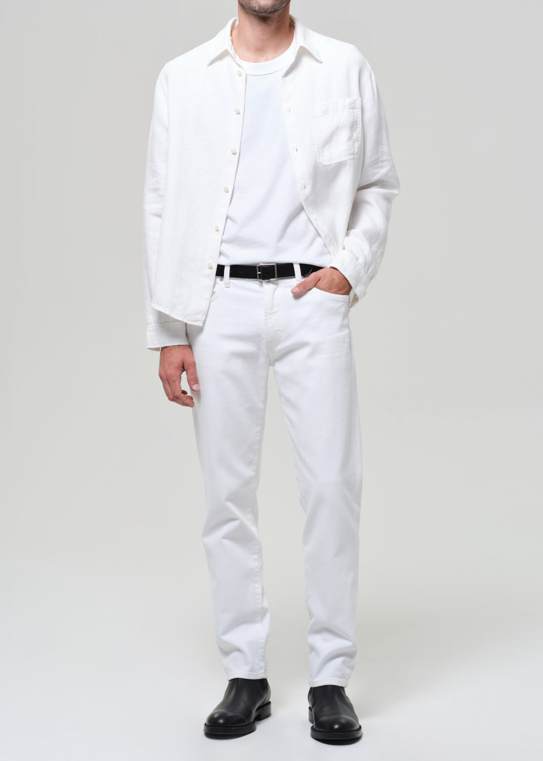 Man wearing a white shirt, white pants, and black shoes on a plain background