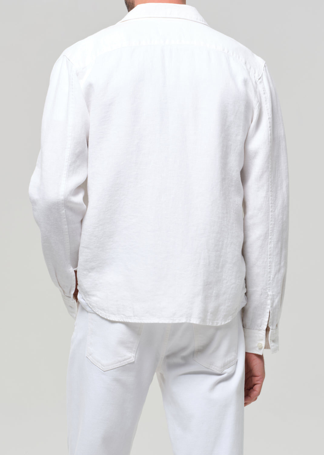 Person wearing a white linen shirt and pants against a plain background